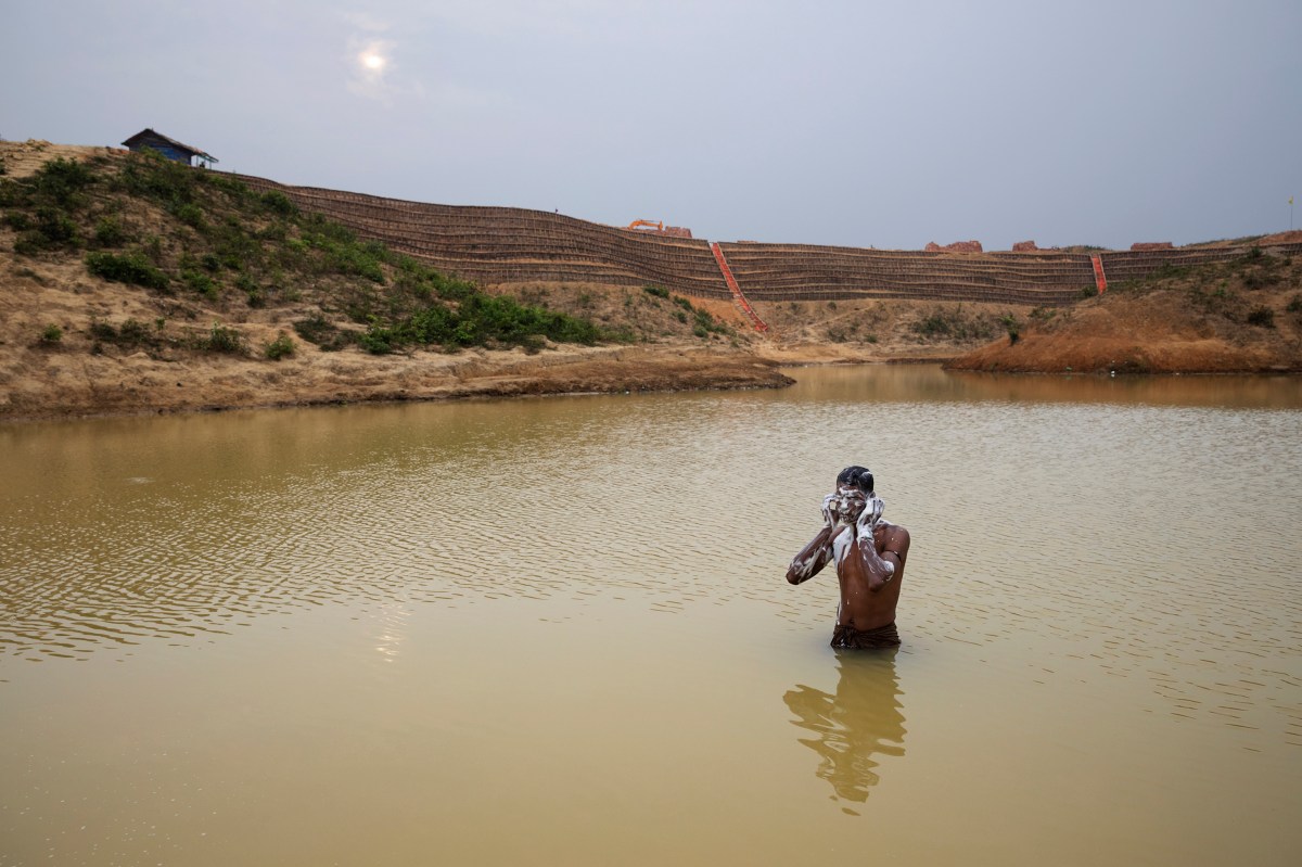 A man bathes in a man-made pond near the camp where he lives. Behind him is the construction of the Camp 20 Extension.