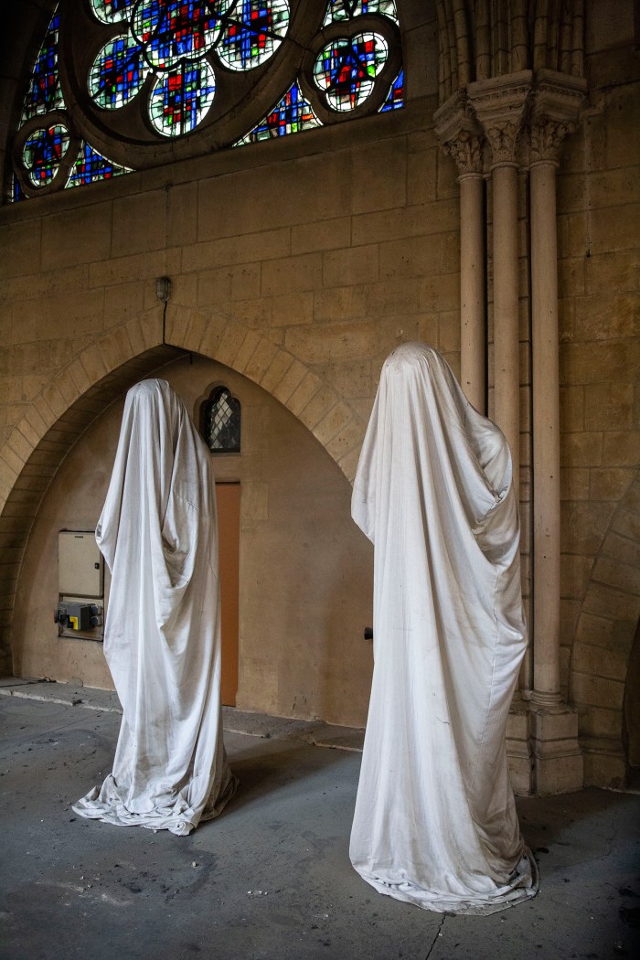 Two statues covered in cloth rest inside the cathedral.